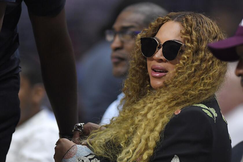 A woman with long hair and sunglasses sits at a sporting event