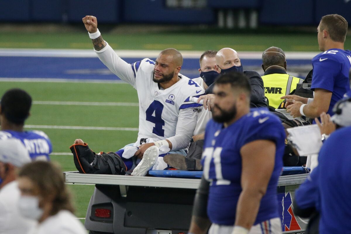 FILE - In this Oct. 11, 2020, file phot, Dallas Cowboys quarterback Dak Prescott (4) lifts his fist to cheers from fans as he is carted off the field after suffering an injury while running the ball during the second half of the team's NFL football game against the New York Giants in Arlington, Texas. The Cowboys are on the verge of a lost year, when they had hoped to contend, after a broken ankle ended the quarterback's season. (AP Photo/Michael Ainsworth, File)