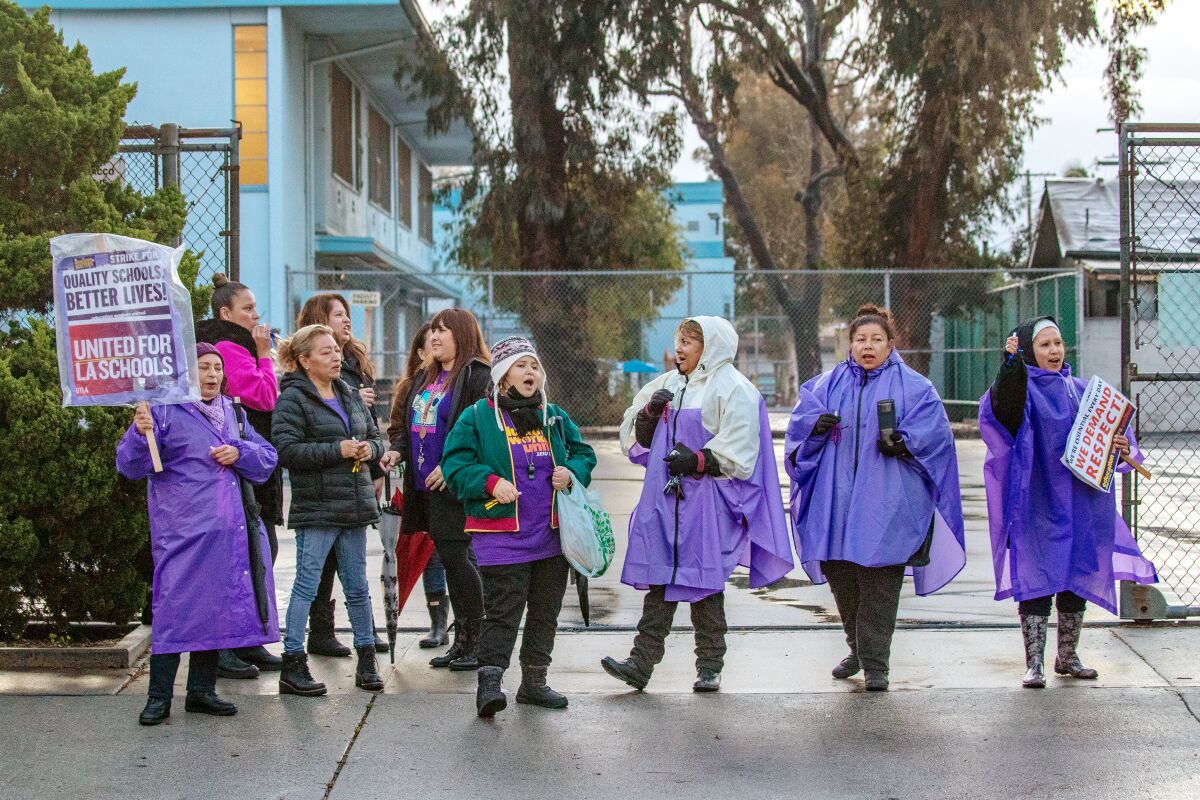 Yadira Martinez, in a purple poncho, stands with others in a picket line in front of a school. 