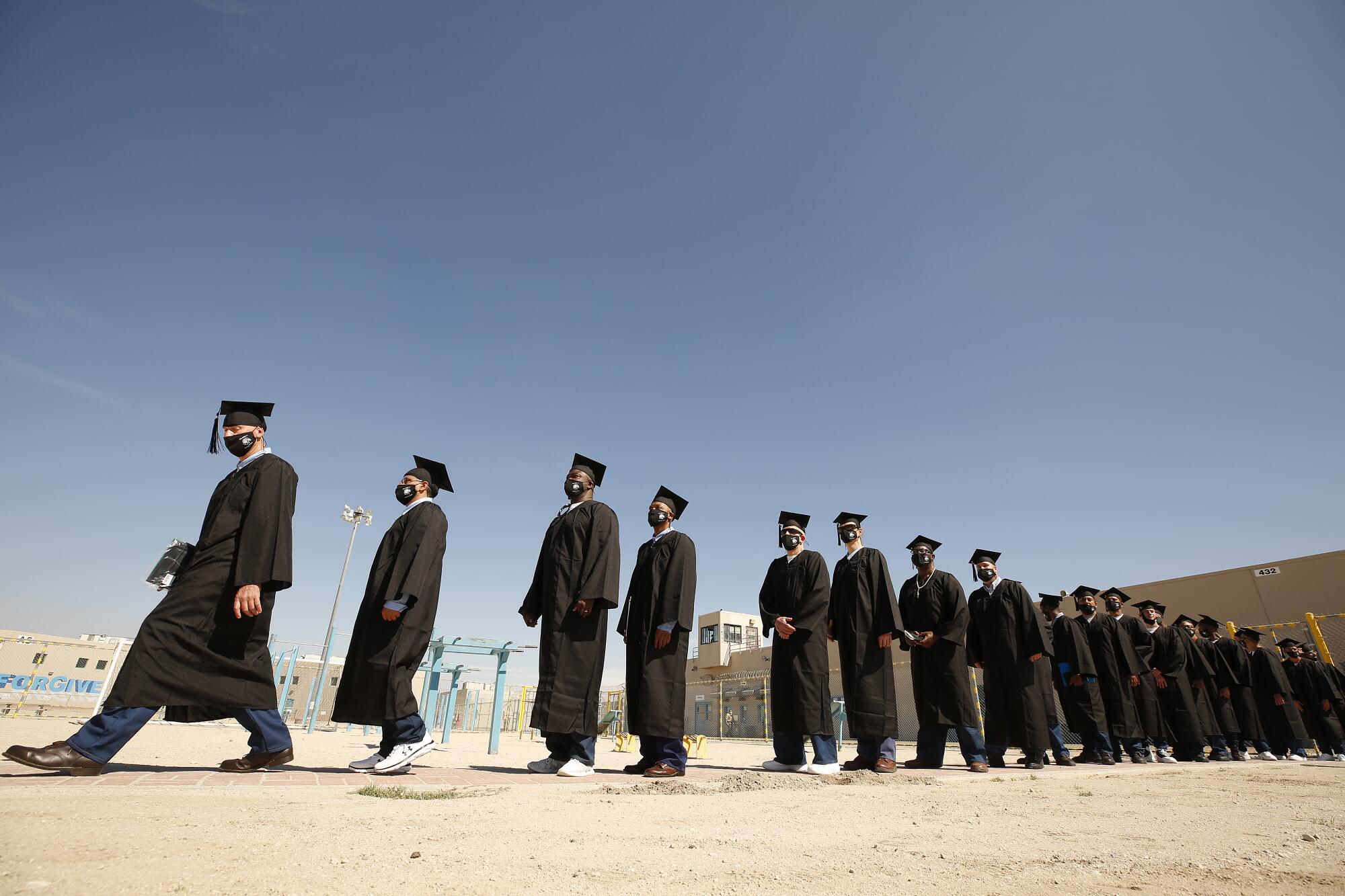 Men wearing graduation robs and hats walk in a prison yard