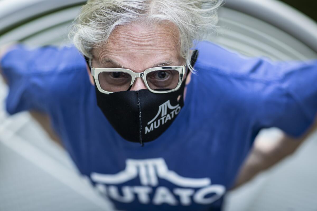 Mark Mothersbaugh wears a mask adorned with the logo of his music production company, Mutato