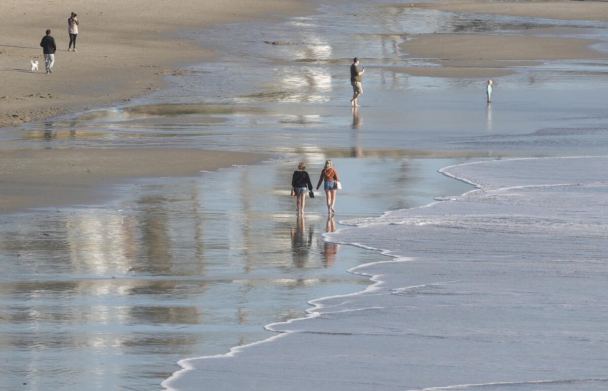 Beachgoers walk in the wet sand exposed.