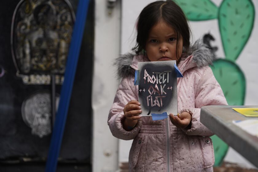 Apache Stronghold member Raetana Manny, 4, shows a sign to save Oak Flat, a site east of Phoenix that the group considers sacred, as she joined a gathering at Self Help Graphics & Art in the Los Angeles neighborhood of Boyle Heights on Monday, March 20, 2023. The Apache group battling a foreign mining firm that wants to build one of the largest copper mines in the United States on what tribal members say is sacred land will get a new chance to make its point Tuesday when a full federal appeals court panel takes another look at the case. (AP Photo/Damian Dovarganes)