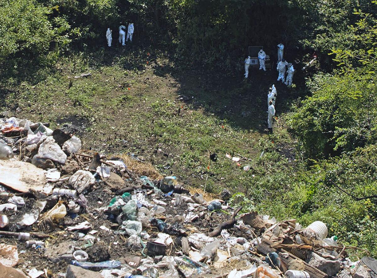 Forensic examiners look for human remains below a garbage-strewn hillside in the densely forested mountains on the outskirts of Cocula, Mexico.