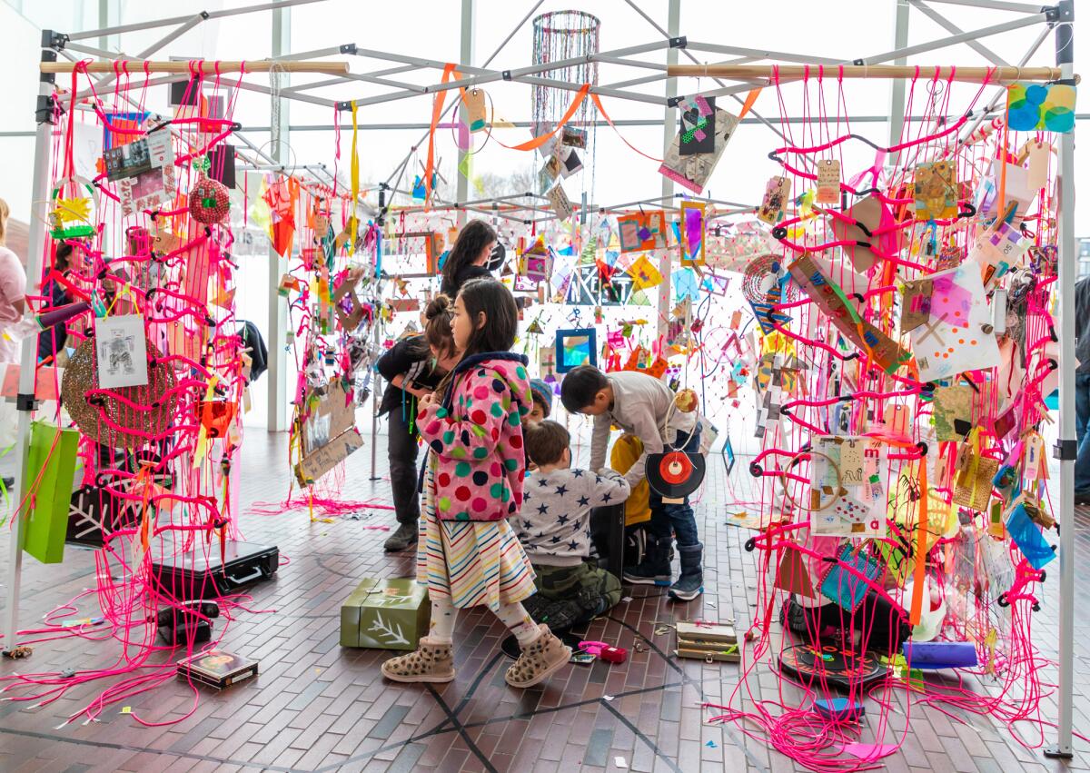 Children walk through a pink string art installation.