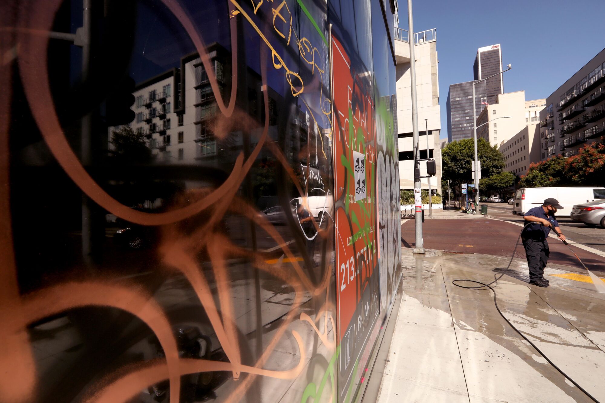 A worker washes off graffiti from the sidewalk on Flower Street next to a building that was tagged Sunday night.