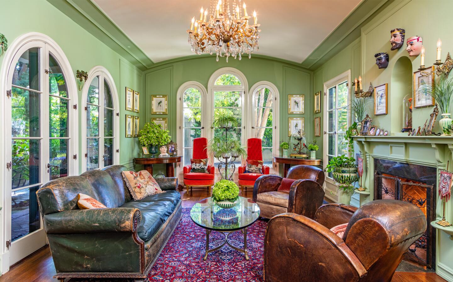 The family room with light green walls, windows overlooking greenery, living room furniture, chandelier and a fireplace.