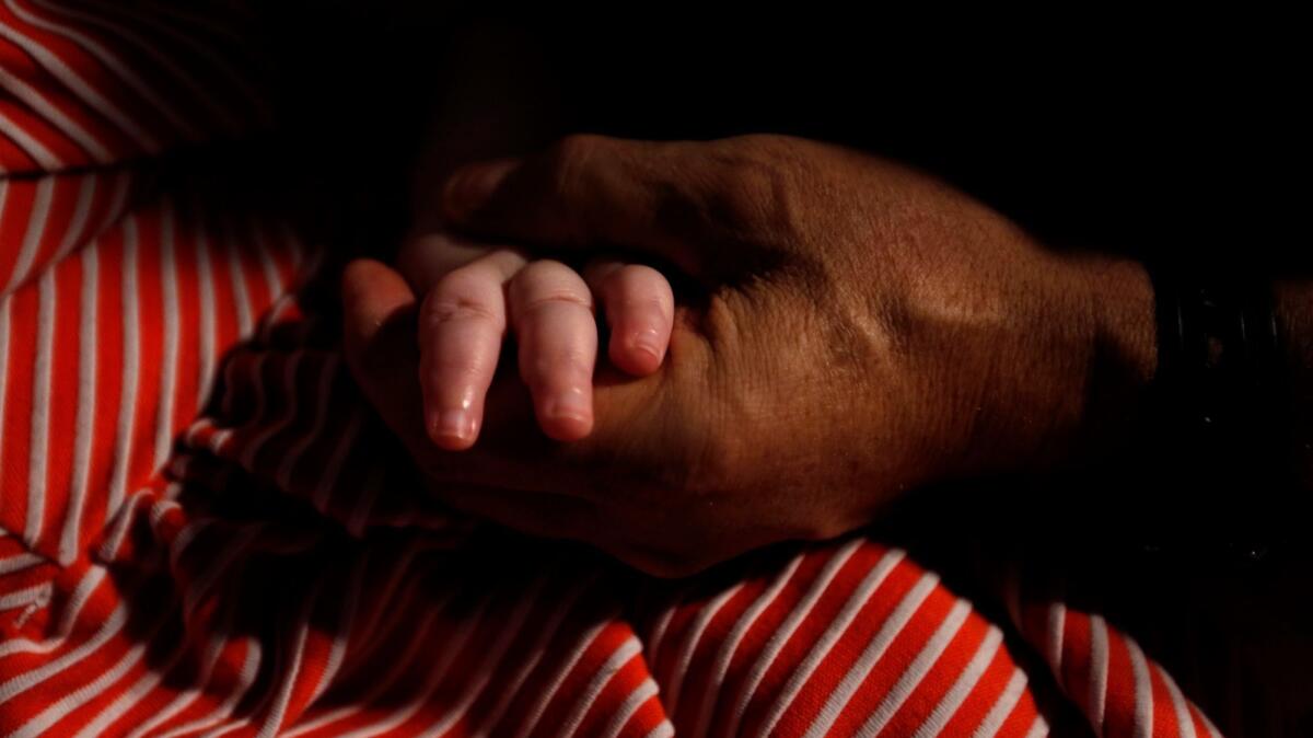 Mohamed Bzeek sostiene la mano de su hija de seis años de edad, que nació con una rara malformación cerebral y no puede ver, oír o hablar. Bzeek cuida hace más de dos décadas a niños en el sistema de adopción con enfermedades terminales (Genaro Molina / Los Angeles Times).