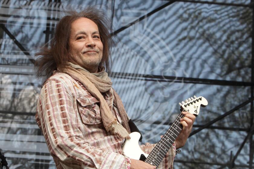 Jake E. Lee plays a bass guitar onstage while smiling