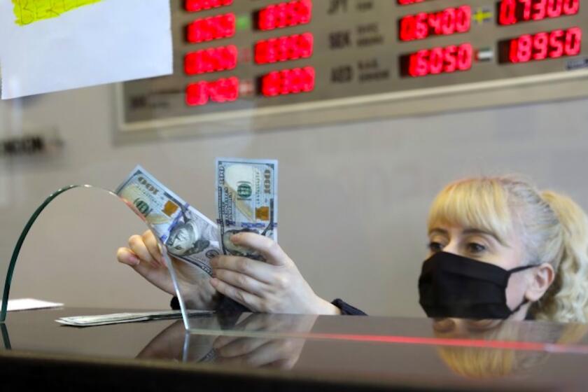 Una empleada con mascarilla sanitaria cambia liras turcas por dólares estadounidenses en una casa de cambio en Ankara, Turquía.