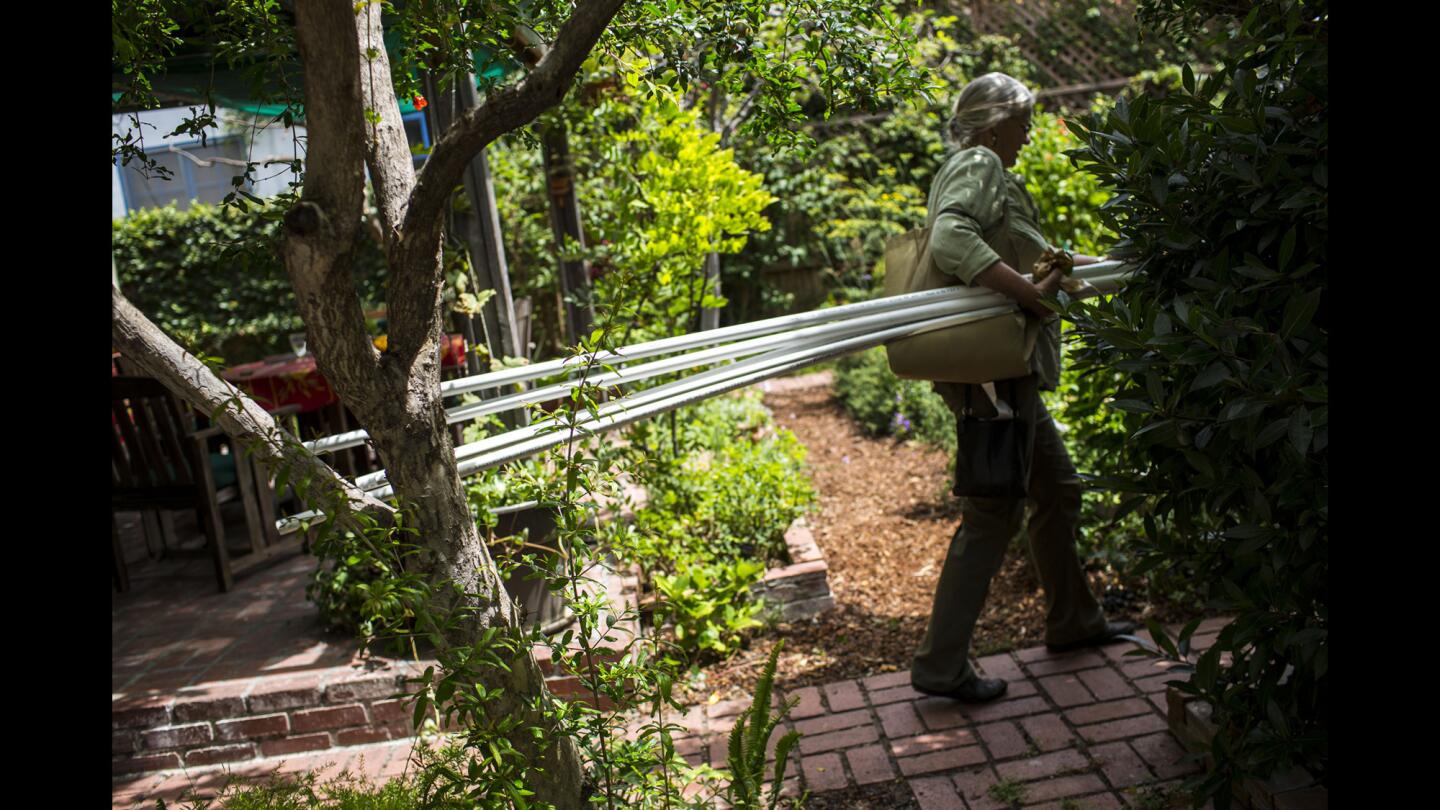 Annie Costanzo carries PVC pipes that will be used to build a gray water system that utilizes runoff water from a washing machine at her home in Los Angeles’ Miracle Mile district.