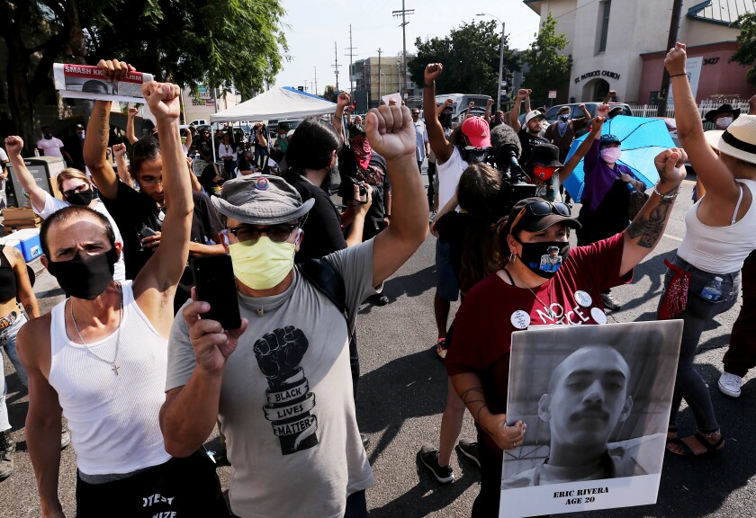 People in masks raise their right fists and hold signs.