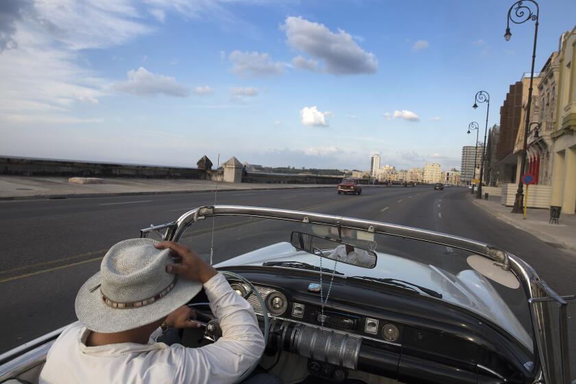 HAVANA, CUBA -- FRIDAY, APRIL 24, 2015: A taxi driver hangs onto his hat while driving his vintage convertible along the Malecon in Havana, Cuba, on April 24, 2015. (Brian van der Brug / Los Angeles Times)