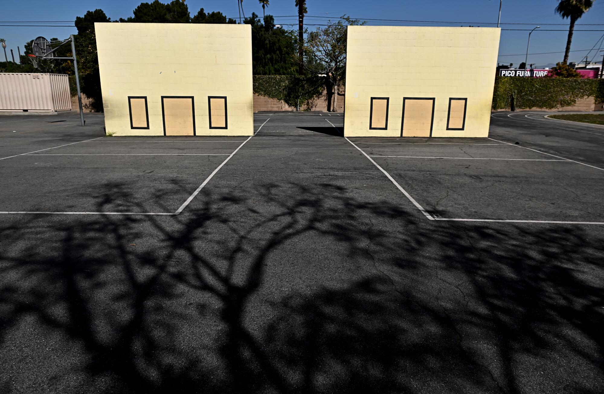 Two yellow walls with rectangles on them on a dark gray asphalt playground.