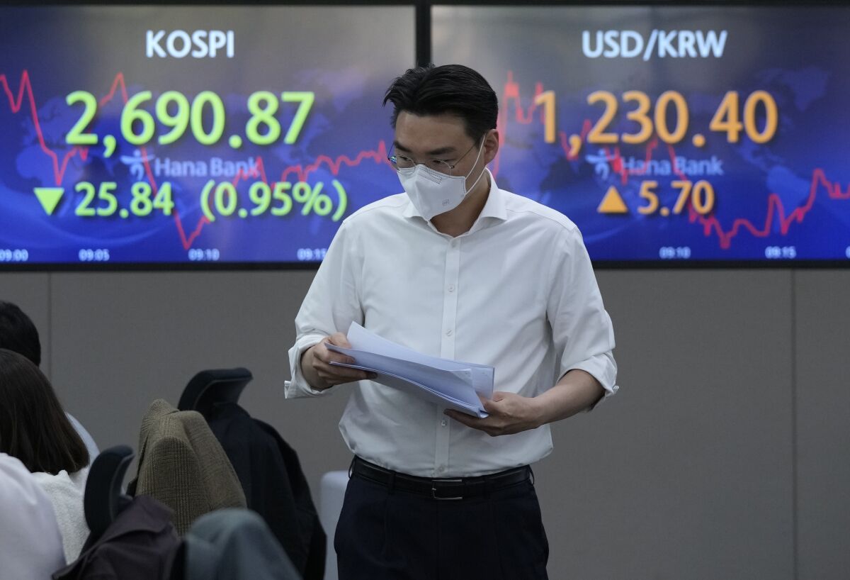 A currency trader passes by screens showing the Korea Composite Stock Price Index (KOSPI), left, and the foreign exchange rate between U.S. dollar and South Korean won, at the foreign exchange dealing room of the KEB Hana Bank headquarters in Seoul, South Korea, Friday, April 15, 2022. Asian shares fell in muted trading as markets remained closed for Good Friday and other holidays. (AP Photo/Ahn Young-joon)