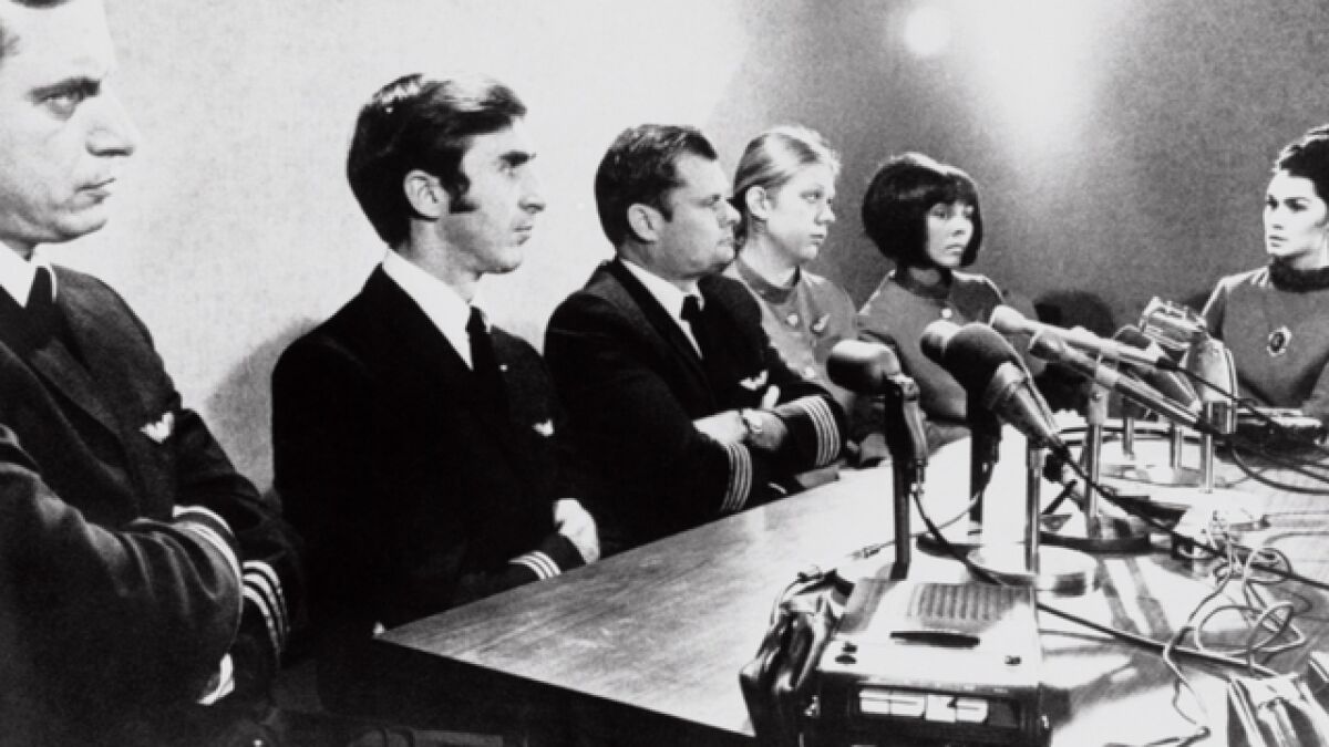 The crew of the plane hijacked by D.B. Cooper sits at a table behind a bank of microphones and a tape recorder.