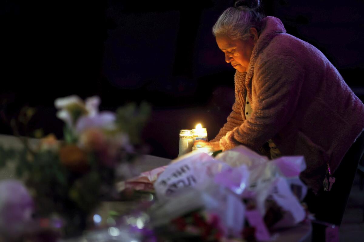 On the right side of the otherwise dark frame, a woman holds a lighted candle in a tall glass. Flowers are in the foreground.