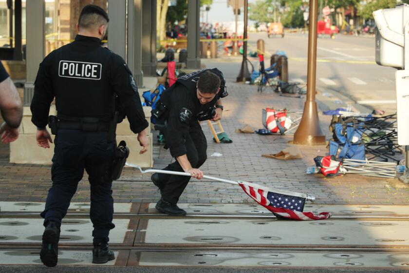 Police officer Johnson picks up a water-logged American flag left behind after yesterday's mass shooting on Tuesday, July 5, 2022 in Highland Park. The area looks like a time capsule as nothing inside the closed area has been removed yet. (Stacey Wescott/Chicago Tribune)