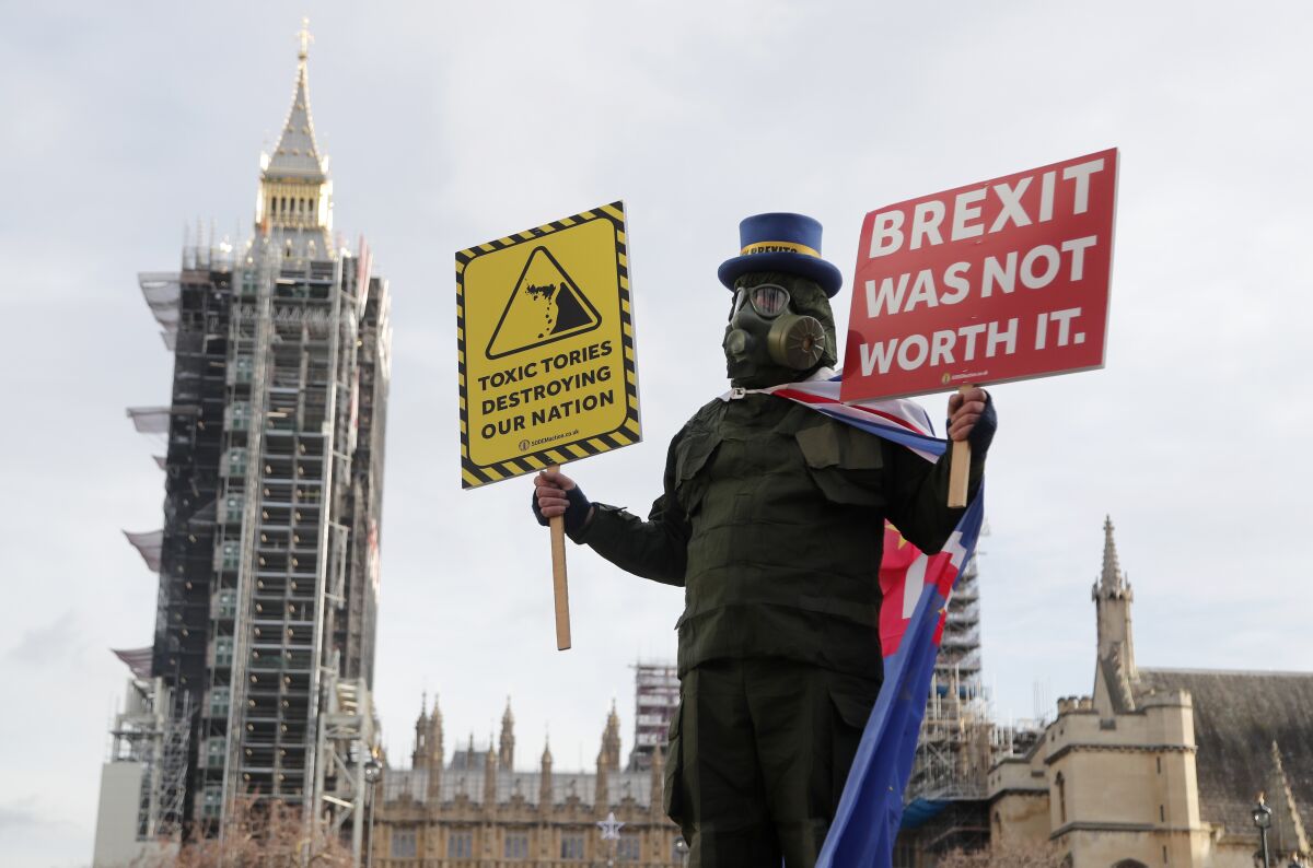 A person in a gas mask with signs that say Toxic Tories destroying our nation, and Brexit was not worth it