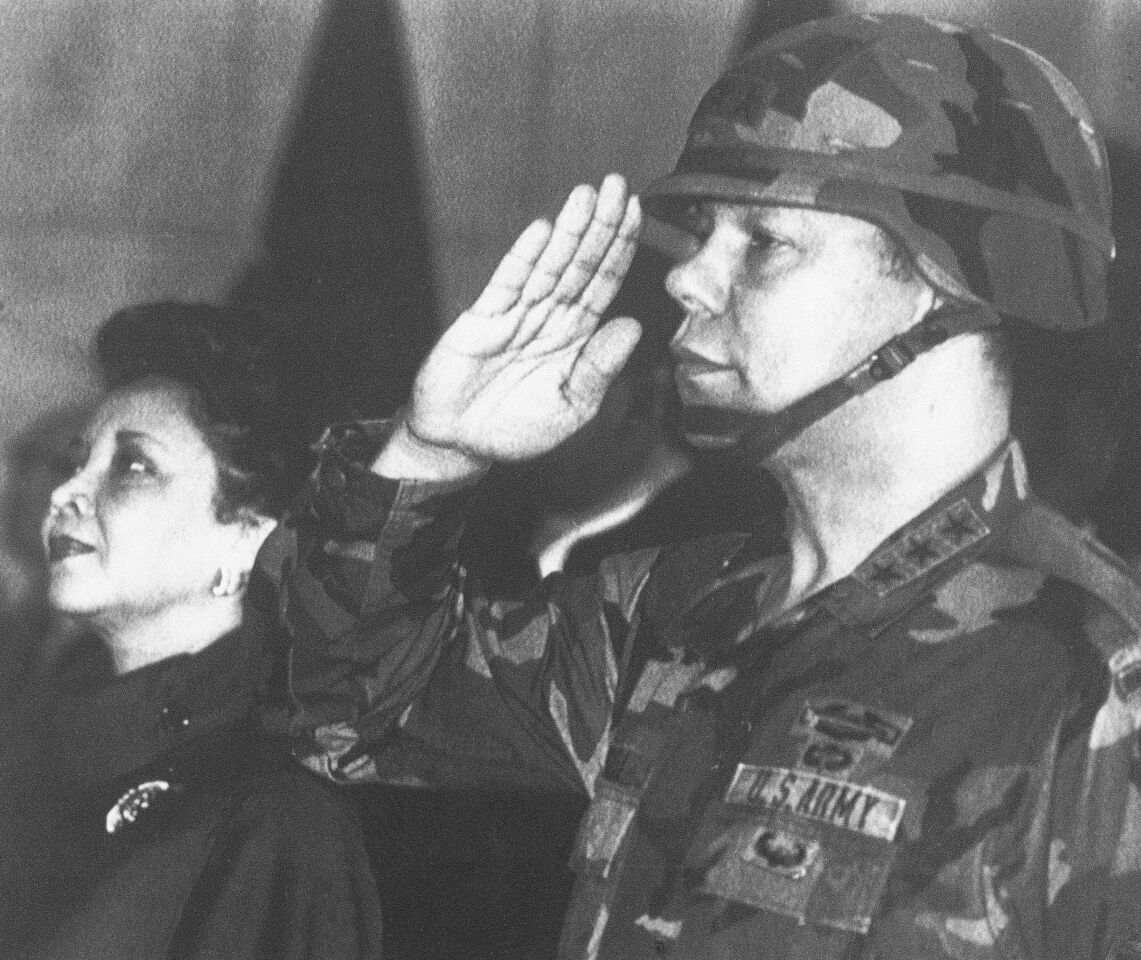 Then Lt. General Colin Powell in uniform salutes and wife Alma stands in attention