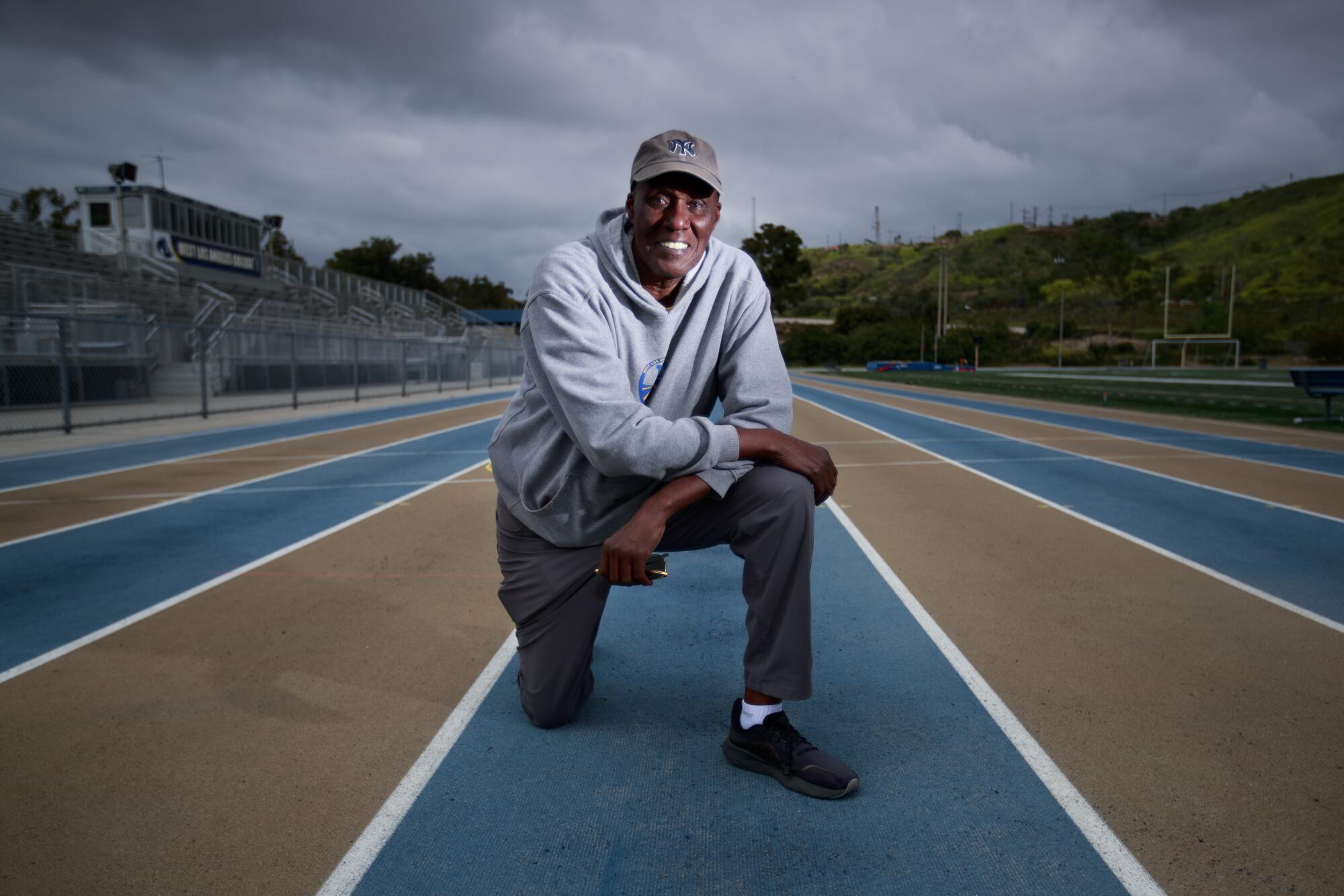 Track coach Bobby Kersee poses for a portrait in a stadium with blue lanes and a cloudy sky overhead.