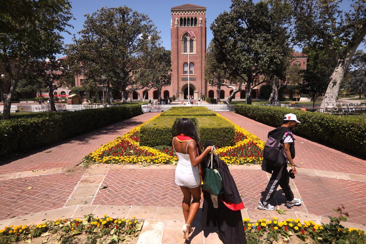 A woman in a dress holds a gown while getting her photo taken on USC's campus