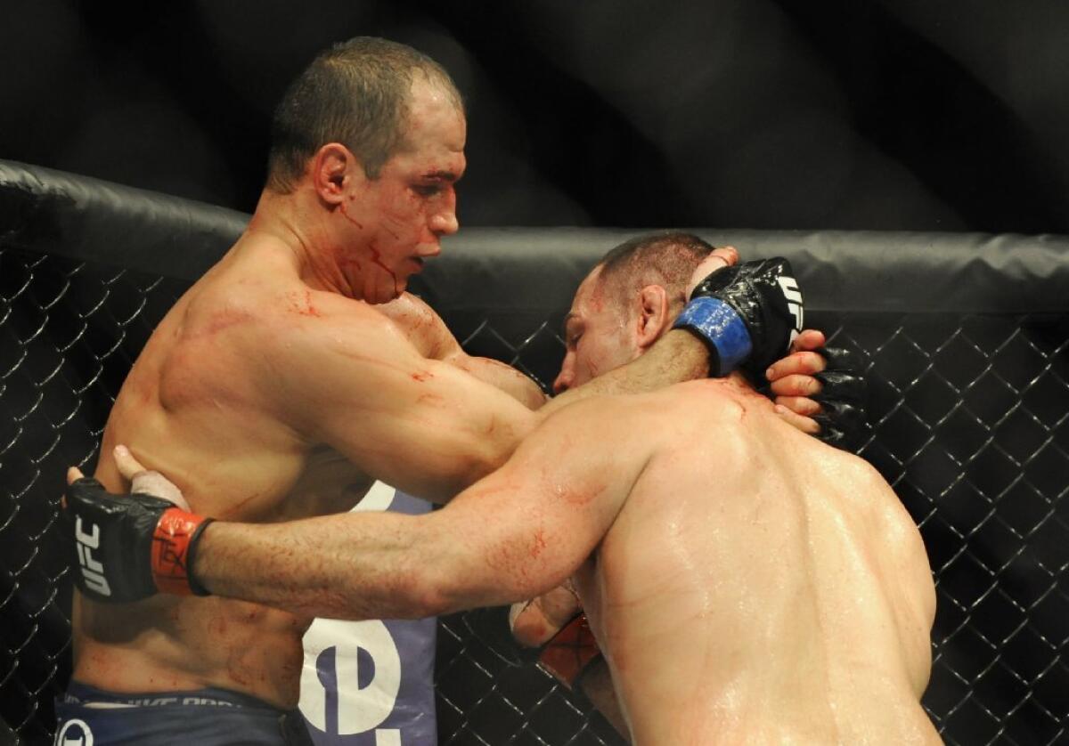 A bloodied Junior Dos Santos, left, tries to hold off Cain Velasquez.
