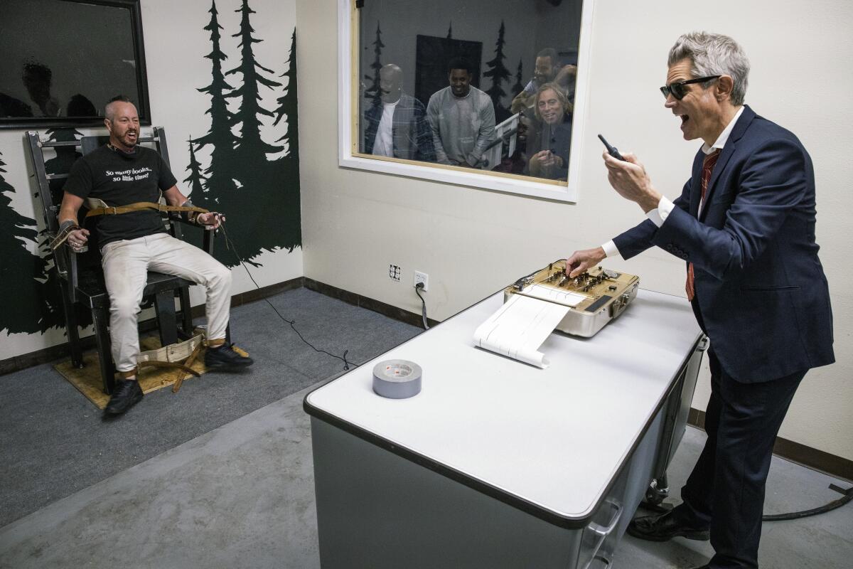 A man strapped into a chair, left, and a man in a suit next to a desk with a machine on it 