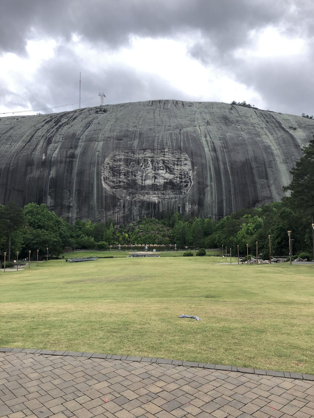 An etching on a bare stone mountain is seen from a distance, across a grassy lawn, on a rainy day.