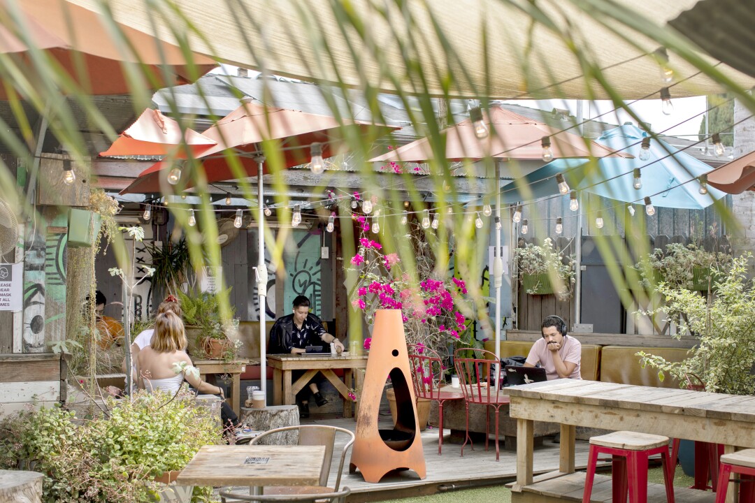 People sit at tables in an outdoor seating area with plants.