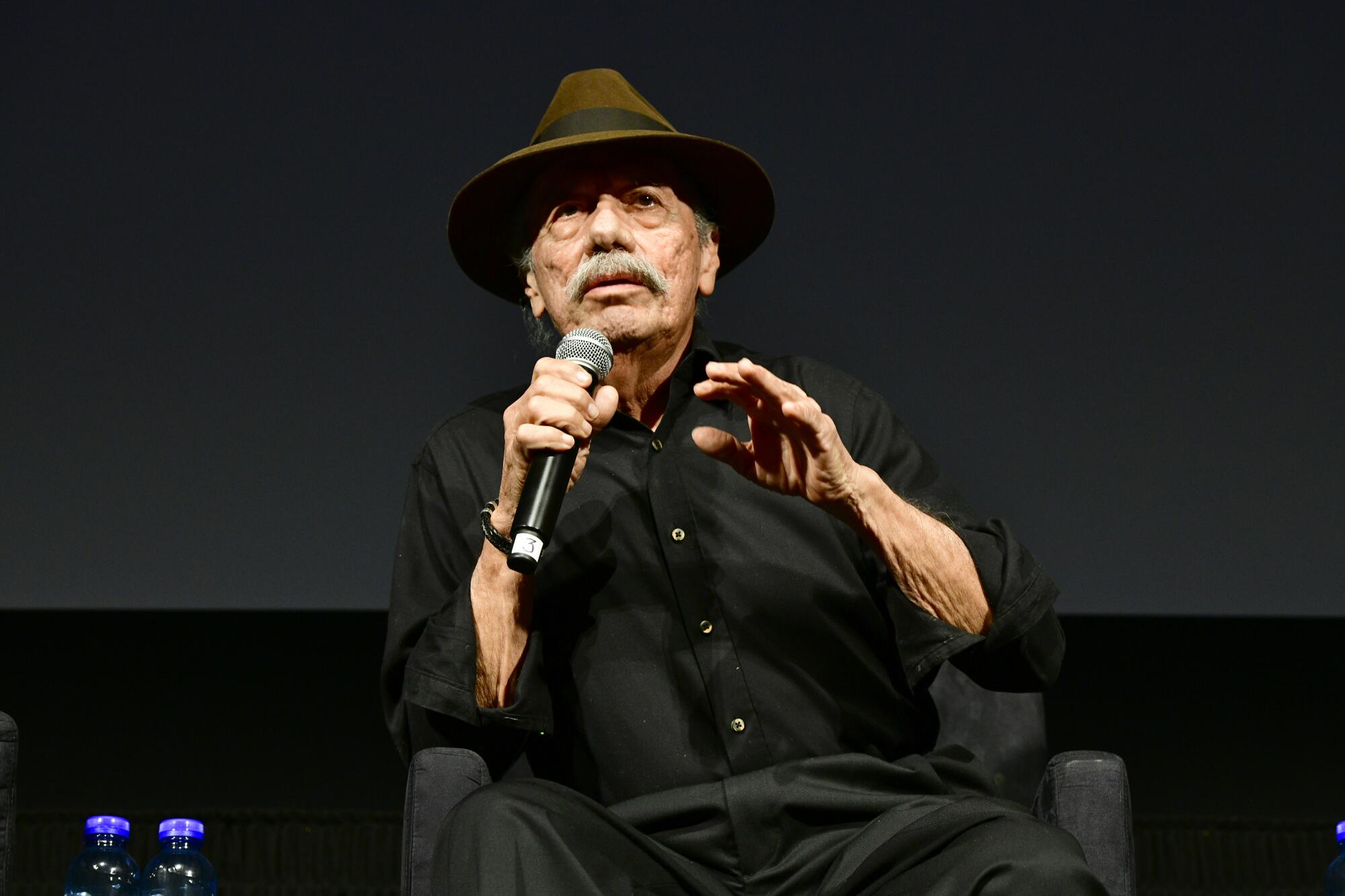 Edward James Olmos sits and holds a microphone