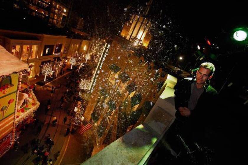 Adam Williams, owner of MagicSnow Systems, stands atop the Cheesecake Factory roof at the Grove during one of the L.A. shopping center's twice daily snow shows that blow snow down on shoppers with MagicSnow equipment.