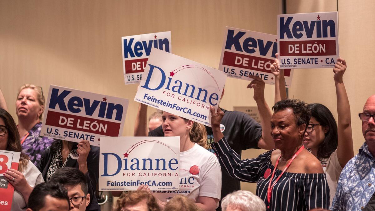 Supporters of Kevin de León and Dianne Feinstein, Democratic rivals in California's senate race, hold signs during a meeting of the California Democratic Party's Women's Caucus this weekend.