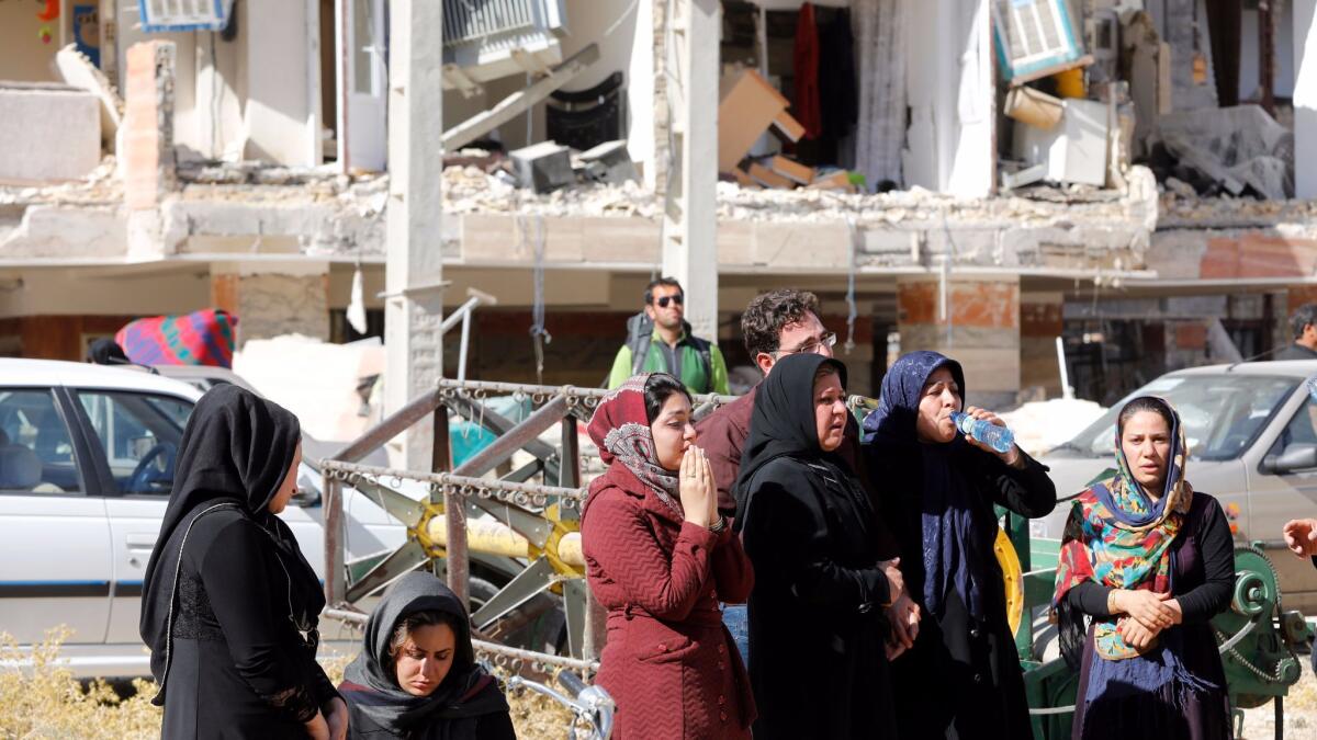 Victims of a powerful earthquake stand outside the wreckage of their home in the city of Pole-Zahab, Iran.