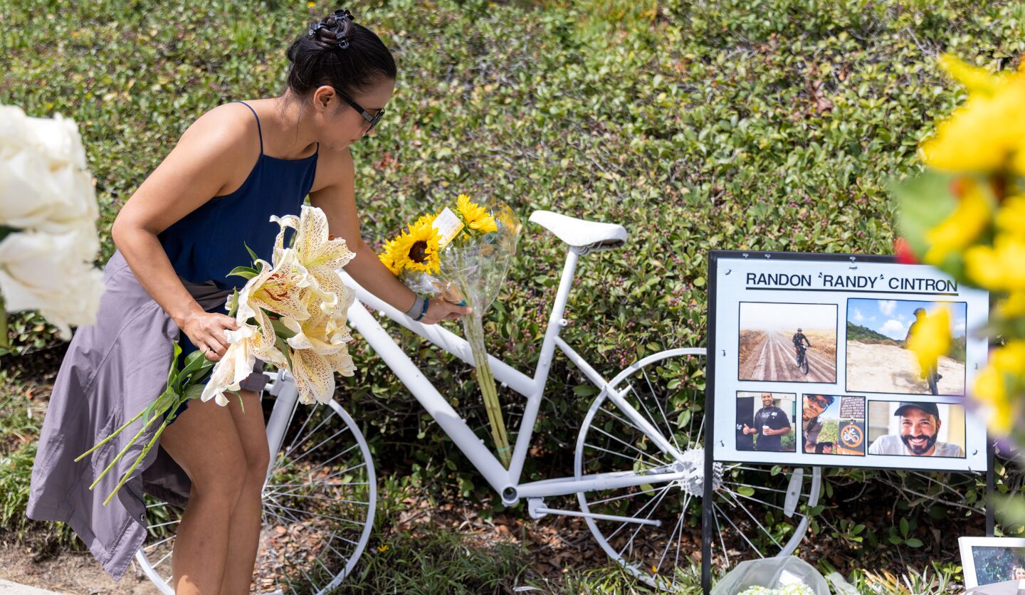 Elaine Canino places flowers on a ghost bike memorializing Randy Cintron on Jamboree Road, where he was struck and killed in a hit-and-run crash in Newport Beach.
