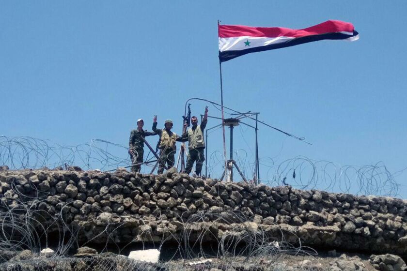 FILE - In this Tuesday, July 17, 2018, file photo, released by the Syrian official news agency SANA, Syrian troops flash the victory sign next to the Syrian flag in Tell al-Haara, the highest hill in the southwestern Daraa province, Syria. Israel shot down a Syrian fighter jet it said had breached its airspace on Tuesday, as Syrian forces reached the Golan Heights frontier for the first time in seven years. (SANA via AP, File)