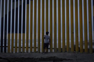 A boy looks through an opening in a border wall with a beach seen on the other side