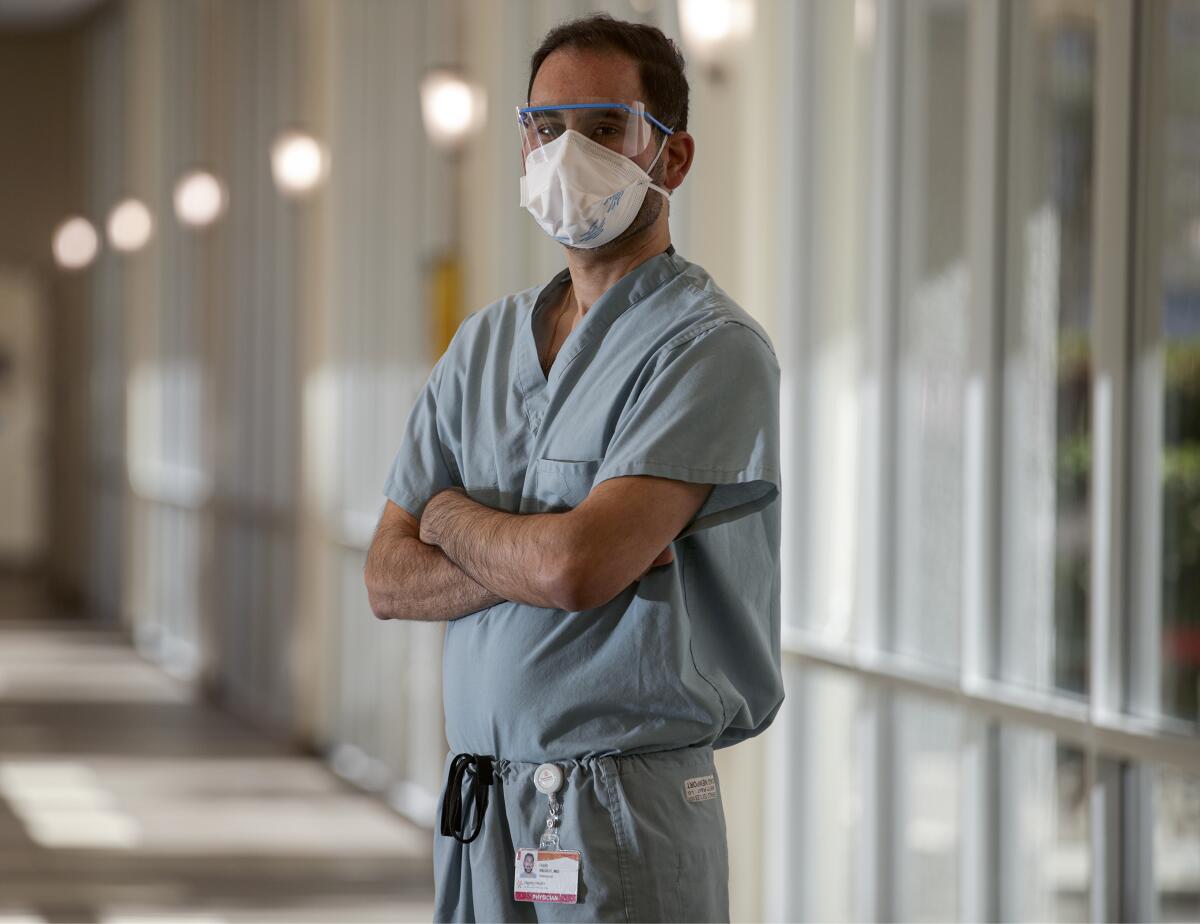 Dr. Hari Reddy stands in a mask stands with his arms folded in a hallway.