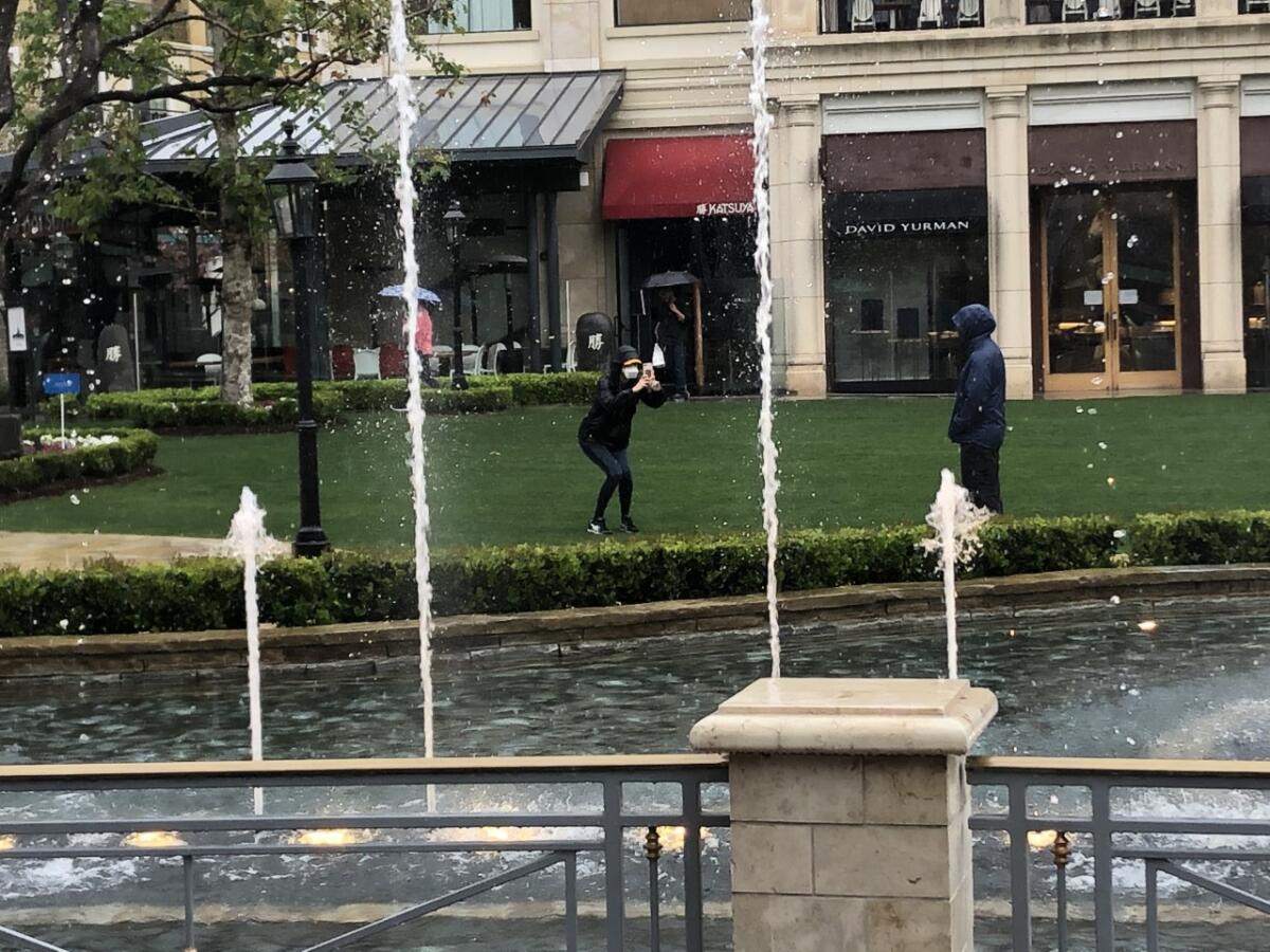 Two individuals wearing facial coverings snap photos in front of the Americana fountain.