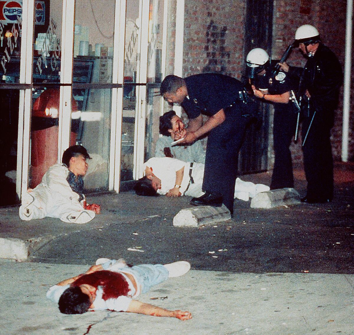 Edward Song Lee, 18, foreground, was shot to death and three other Koreans were injured in an exchange of gunfire with looters at 3rd Street and Hobart Boulevard in Koreatown on April 30, 1992. Police questioned the survivors of the attack who were shot while trying to protect a Korean-owned pizza parlor. (Hyungwon Kang / Los Angeles Times)