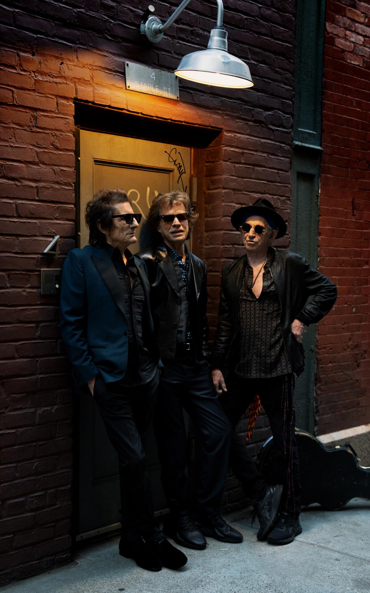 Three old rock musicians standing in front of a brick wall