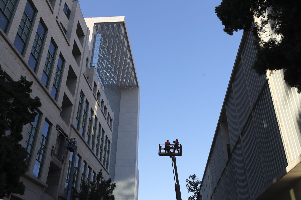Workers in a cherry-picker are silhouetted against the sky where the pedestrian bridge had stretched across Union Street between the Hall of Justice, left, and the old county courthouse. The newer Central Court looms in the background above both buildings.