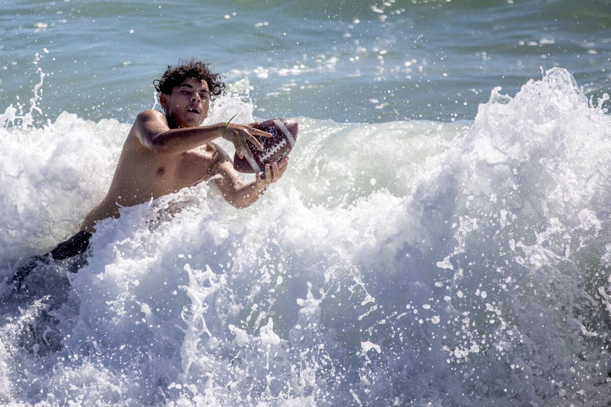 A boy dives into a crashing wave to catch a football