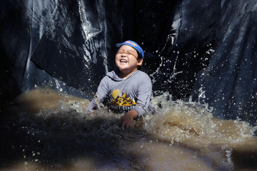 Minjun Chang, 7, of South Pasadena, is all smiles as he splashes into muddy water on the "mud slide" during the opening day of Adventure Playground in Huntington Beach on Saturday, June 24, 2023. Adventure Playground is a place where kids can play in a lagoon, slide down a mudslide, race boats and just be a kid. (Photo by James Carbone)