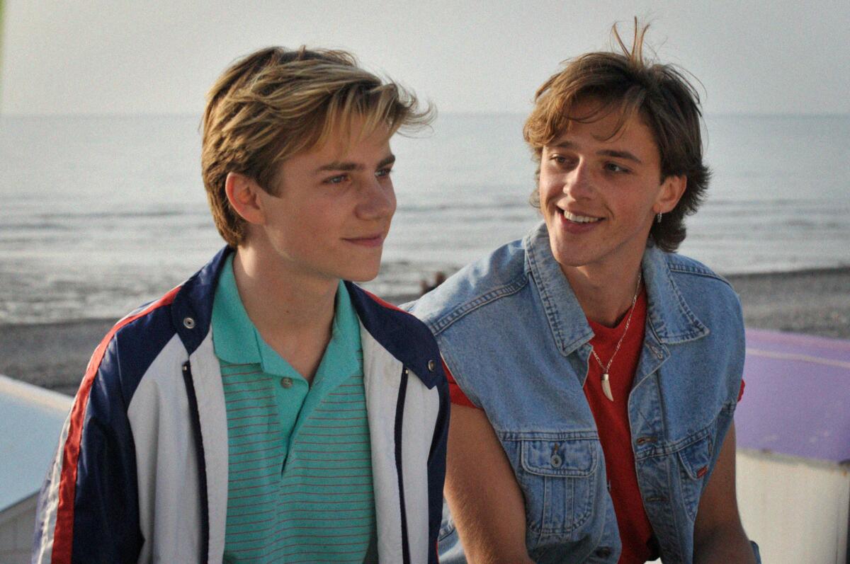 Two young men sit on a beach