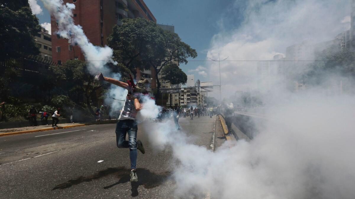 A protester throws back a tear gas grenade launched by police during a street clash Saturday in Caracas.