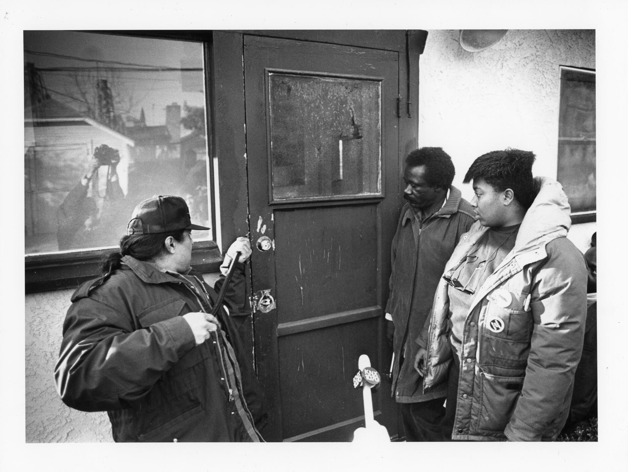 A man tries to pry open a door as two other people watch.