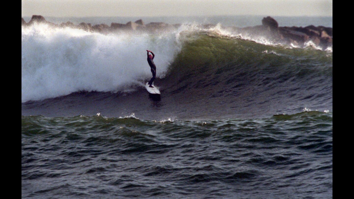 A surfer throws up his arms after catching a double-overhead wave at Cloudbreak, south of the Seal Beach Pier.