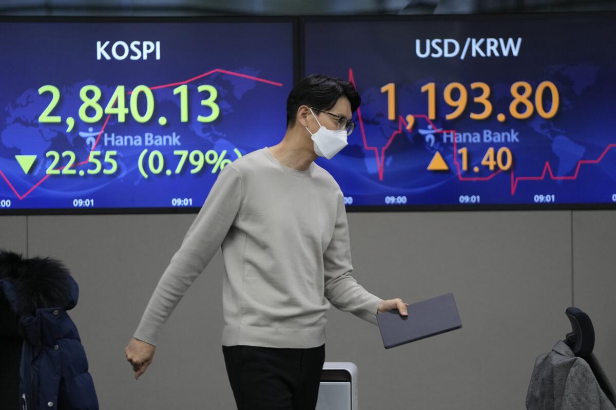 A currency trader walks by the screens showing the Korea Composite Stock Price Index (KOSPI), left, and the foreign exchange rate between U.S. dollar and South Korean won at a foreign exchange dealing room in Seoul, South Korea, Friday, Jan. 21, 2022. Shares were lower in Asia on Friday after a late afternoon sell-off wiped out gains for stocks on Wall Street. (AP Photo/Lee Jin-man)