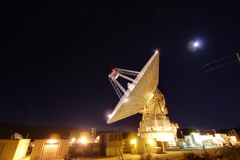 A massive antenna is illuminated against the night sky 